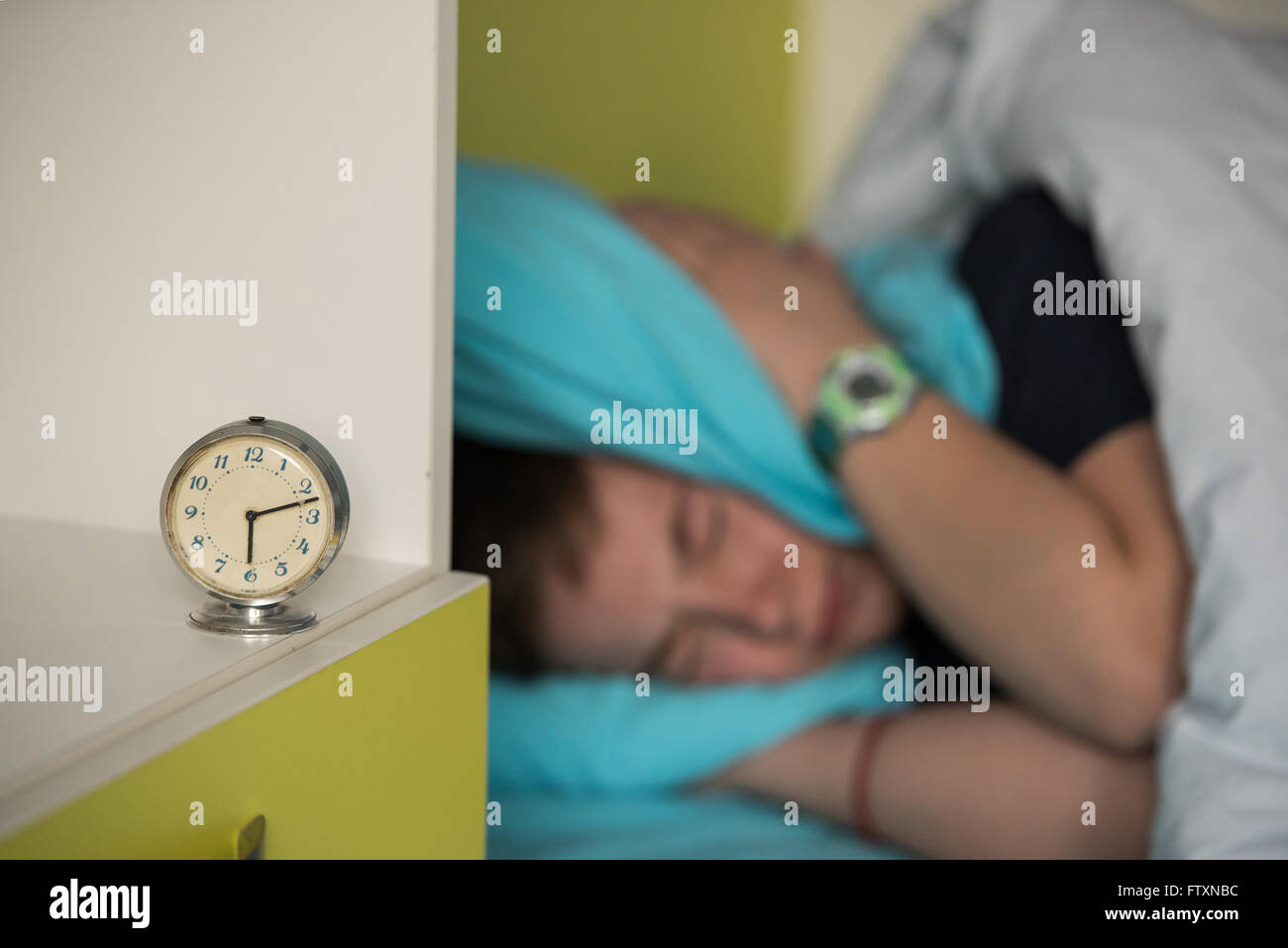 Boy in bed covering his ears while alarm ringing Stock Photo