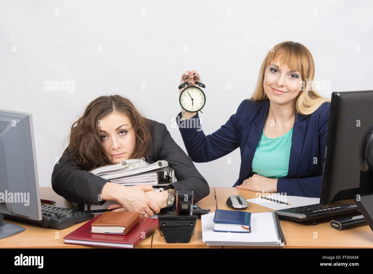 The girl in the office with a smile shows the time on the clock next to