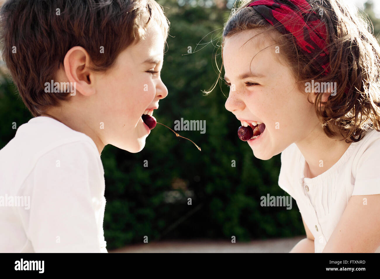 Boy and girl face to face eating cherries Stock Photo