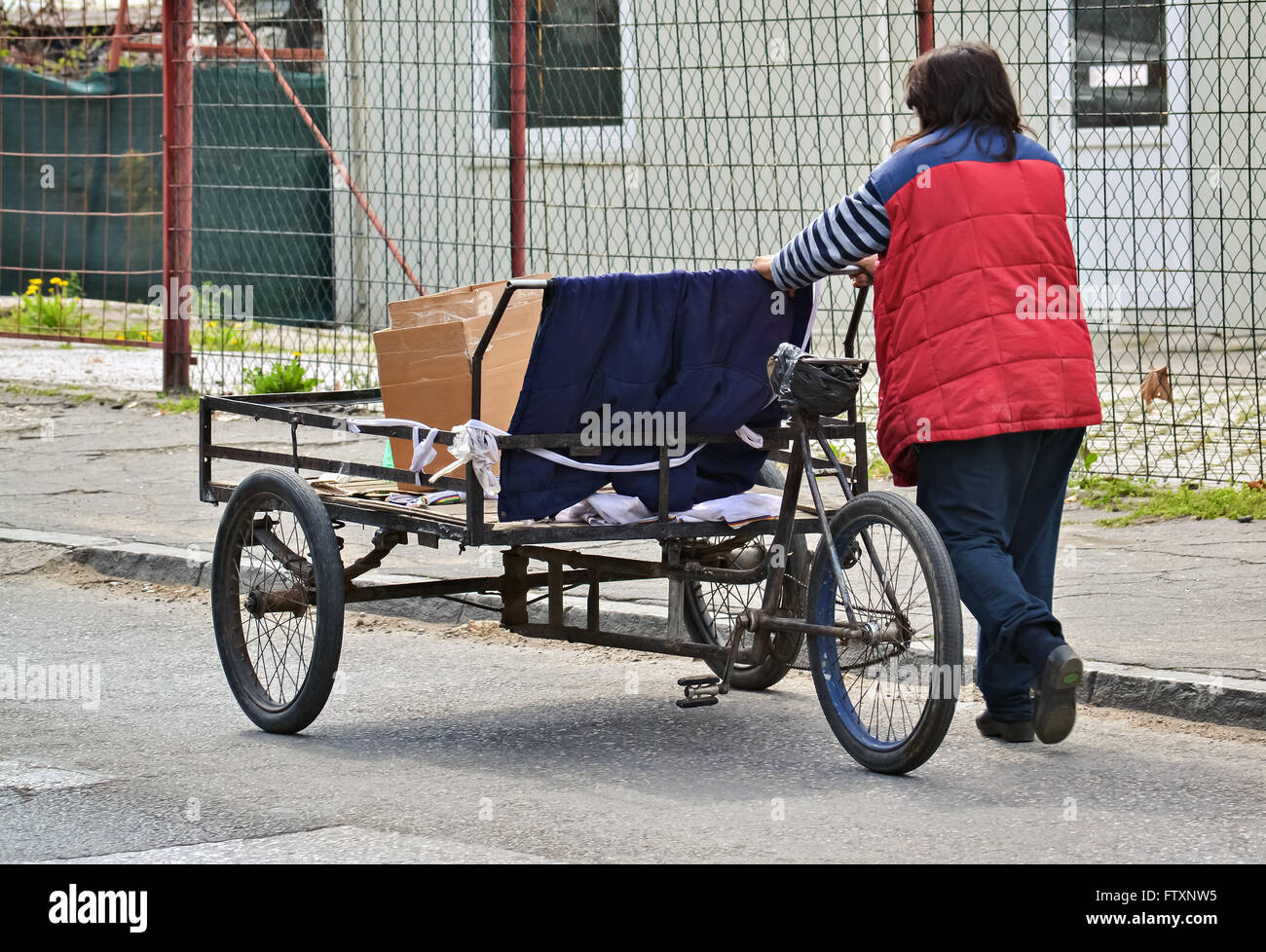 Poor woman pushing an old three wheel cart on the street Stock Photo