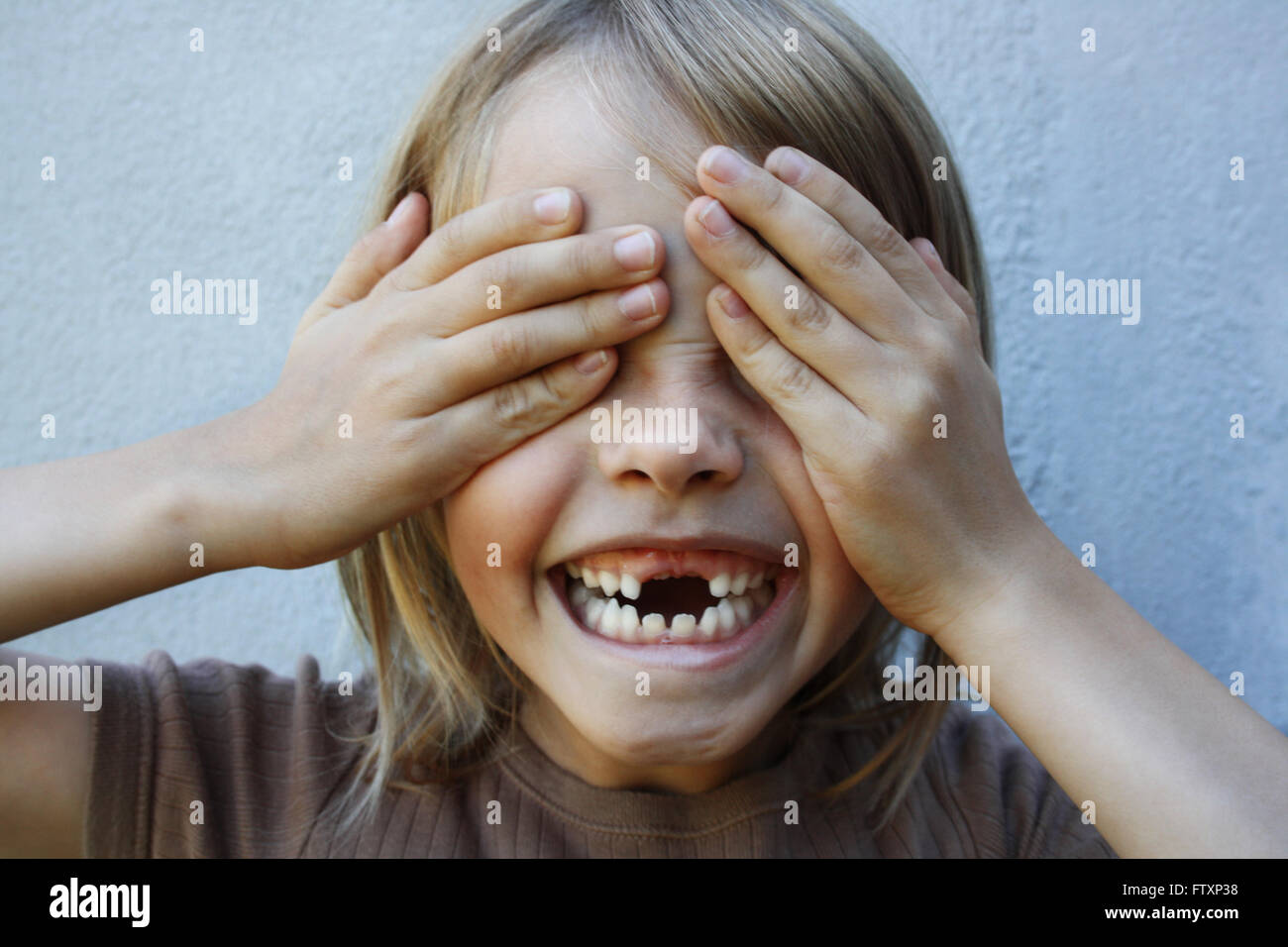Boy with gap toothed smile with hands covering eyes Stock Photo