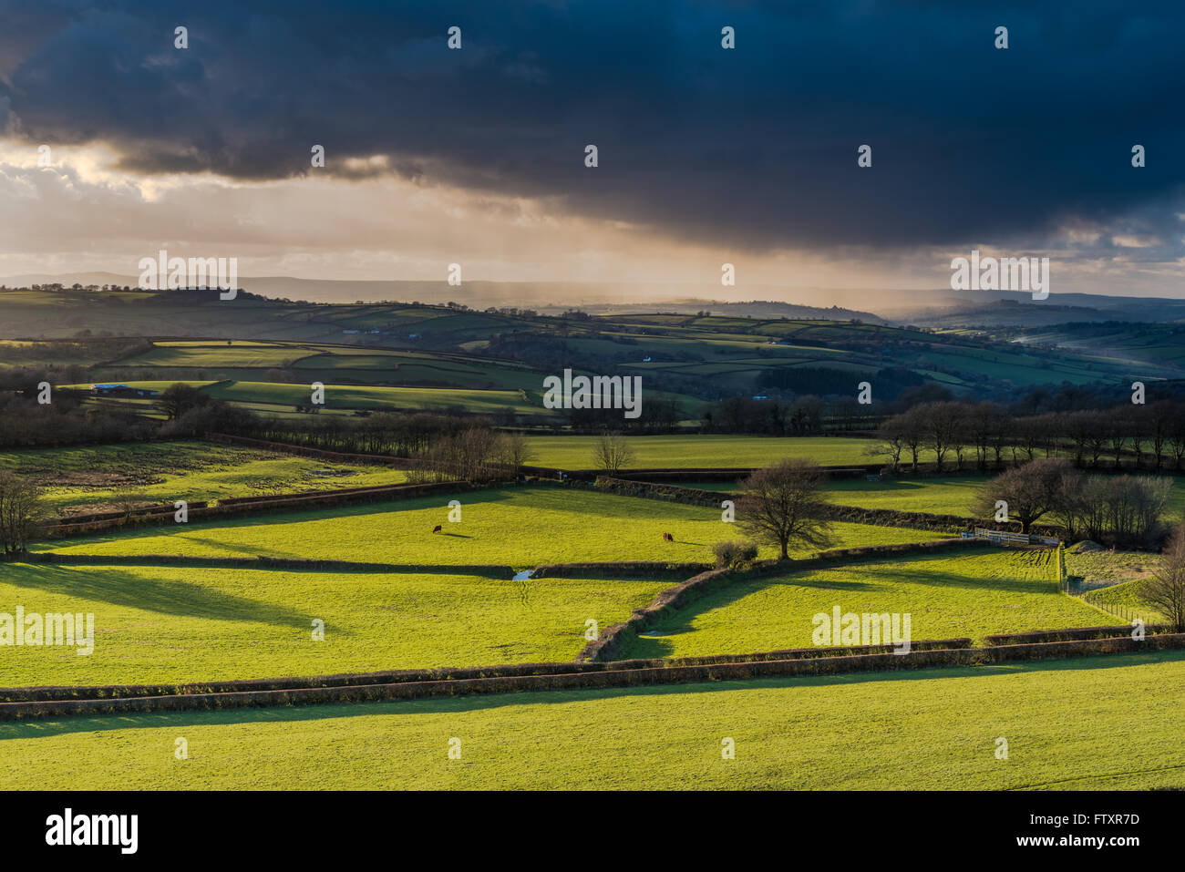 Farmland and coutryside with stormy clouds rolling with pouring rain at sunset. View from hill top, long shadows. Stock Photo