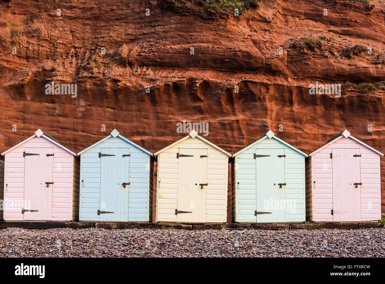 Beach hut row in pastel colors, red rock background, South Devon, UK Stock Photo