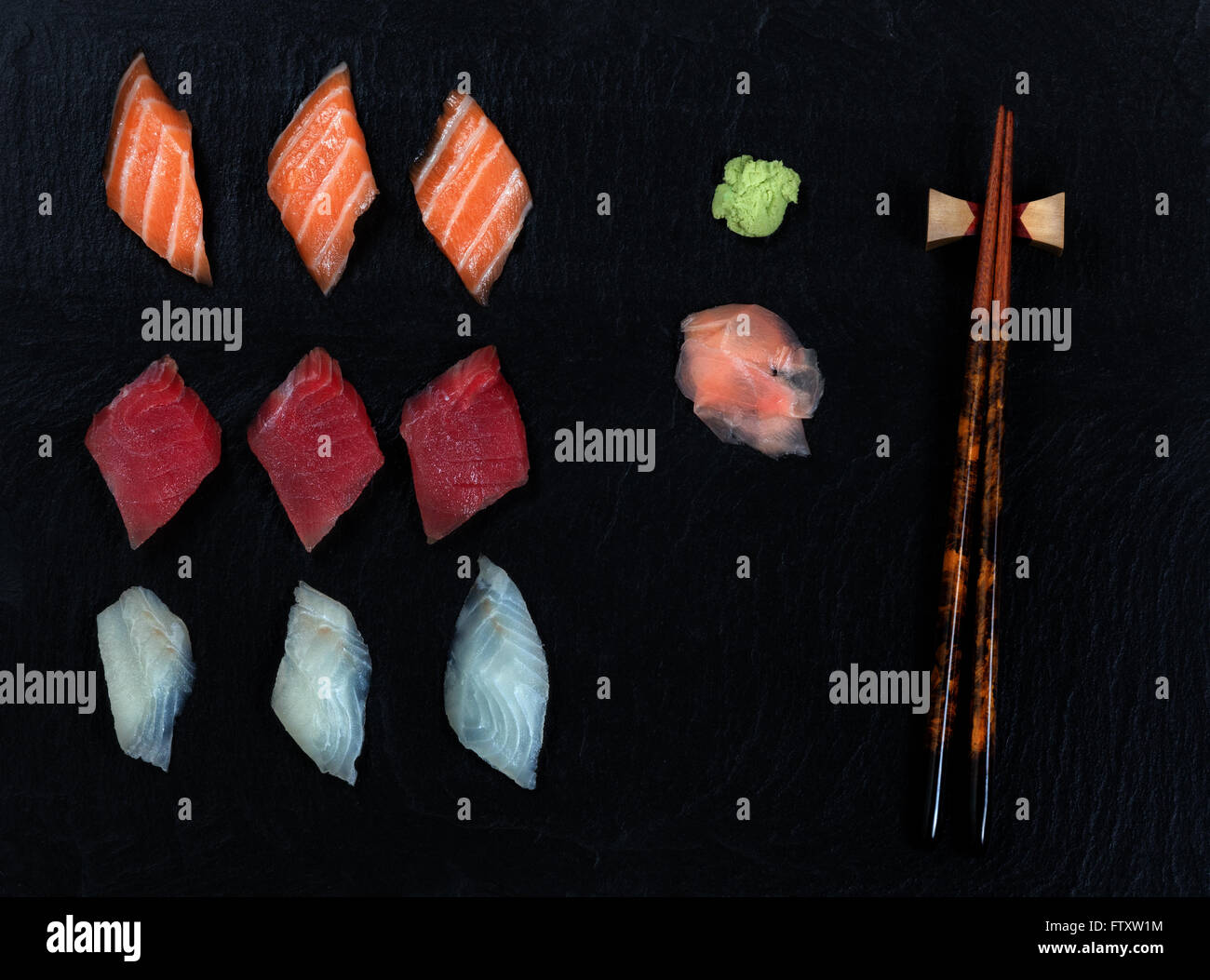 Overhead view of fresh Japanese sushi, ginger, wasabi, and chopsticks on black slate. Stock Photo