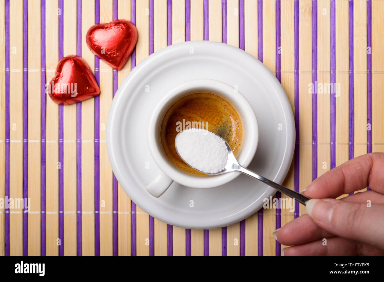 female hand with a teaspoon of sugar to sweeten a cup of coffee and two chocolate heart Stock Photo