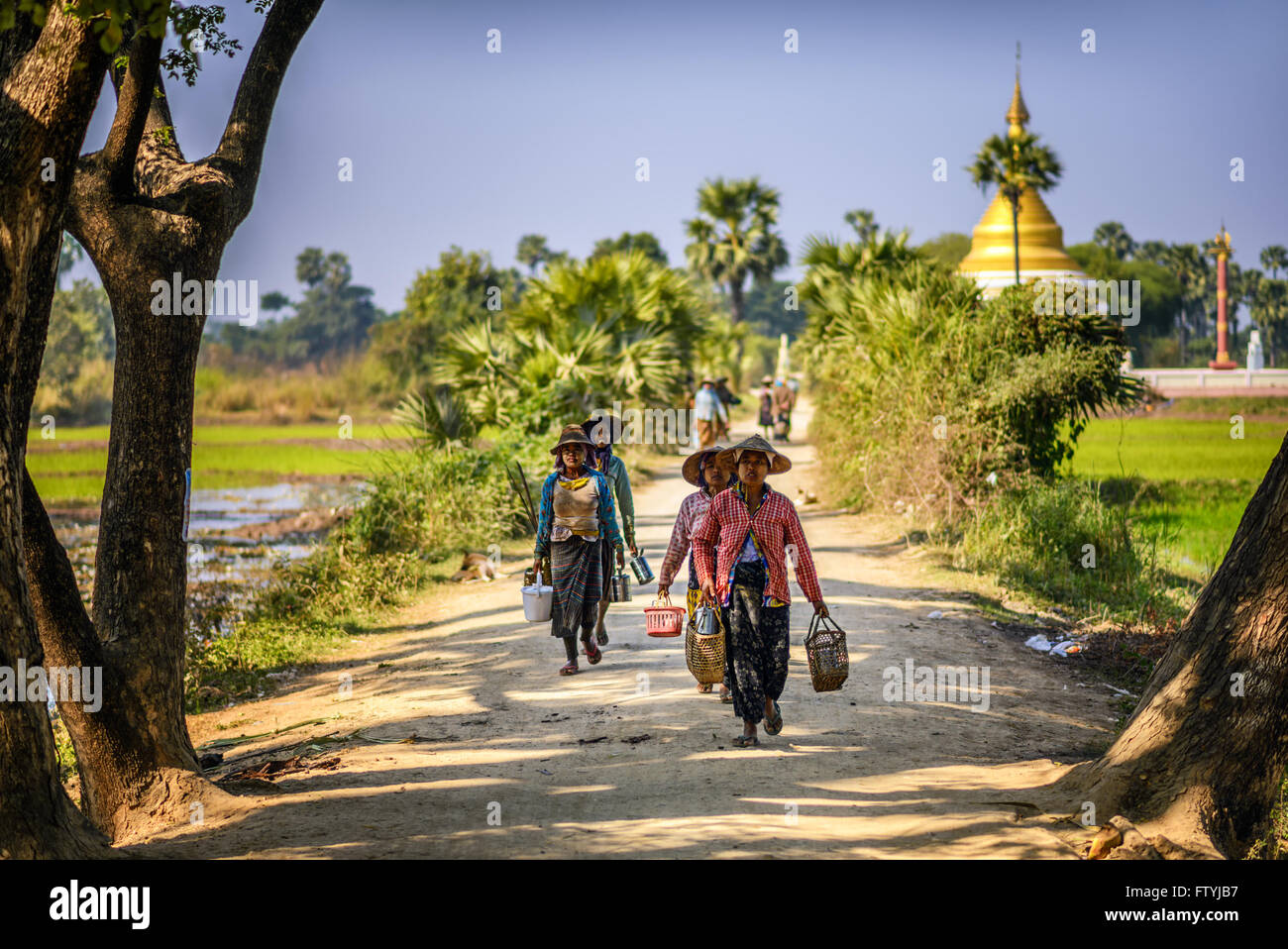 Female farmer workers in traditional straw wide-brimmed hats walk near a buddhist Stupa in Mandalay, Myanmar Stock Photo