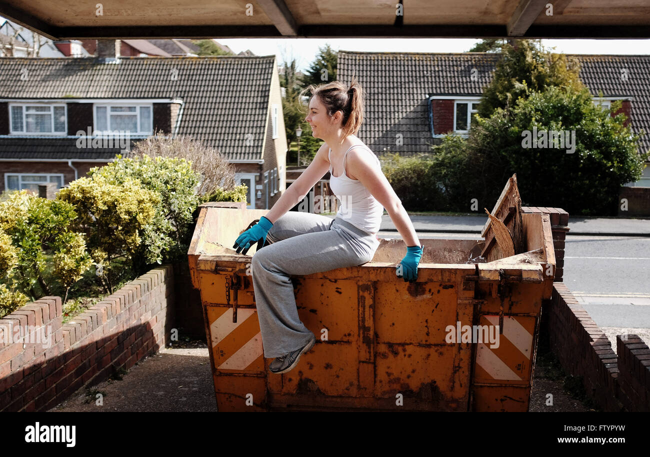 Young woman in her 20s doing DIY climbing out of a builders rented skip Stock Photo