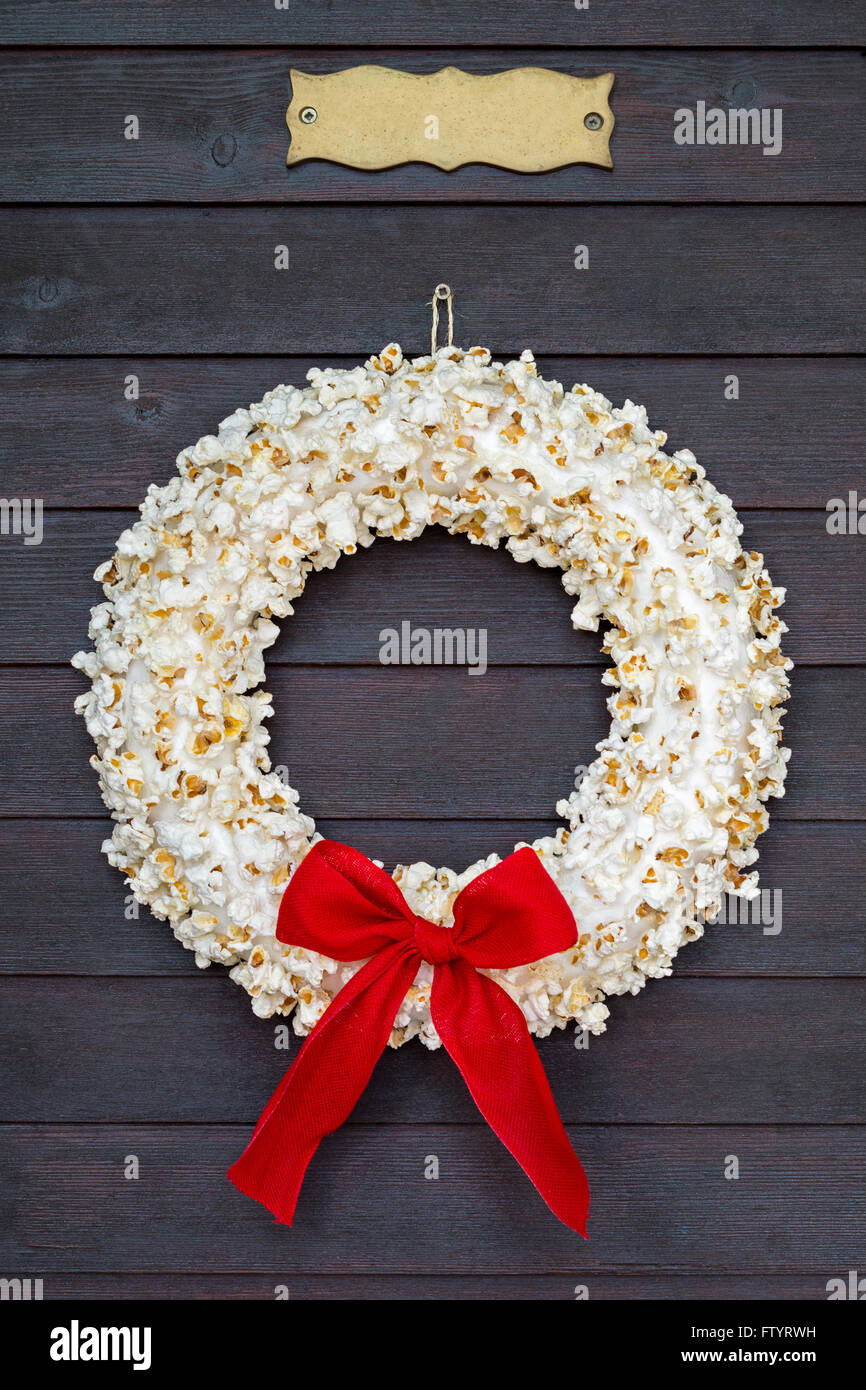 Popcorn wreath with red bow hanging on dark wooden door with name plate. Stock Photo