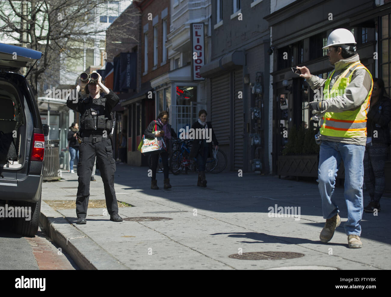 Washington, District of Columbia, USA. 30th Mar, 2016. 'A construction worker takes a photo of a Secret Service Agent using a pair of binoculars as she keeps an eye on activity along 14th Street as President Barack Obama has lunch with formerly incarcerated individuals who have received commutations at Bus Boys and Poets restaurant in Washington, DC on March 30, 2016. Obama commented 61 sentences today. Credit: Kevin Dietsch/Pool via CNP © Kevin Dietsch/CNP/ZUMA Wire/Alamy Live News Stock Photo