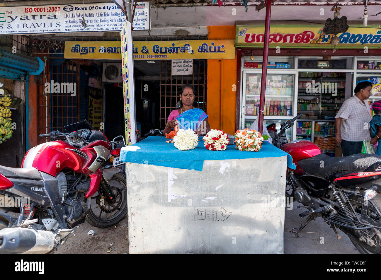 Woman selling flowers from a roadside stall in front of shops at Kalpakkam , Tamil Nadu, India Stock Photo
