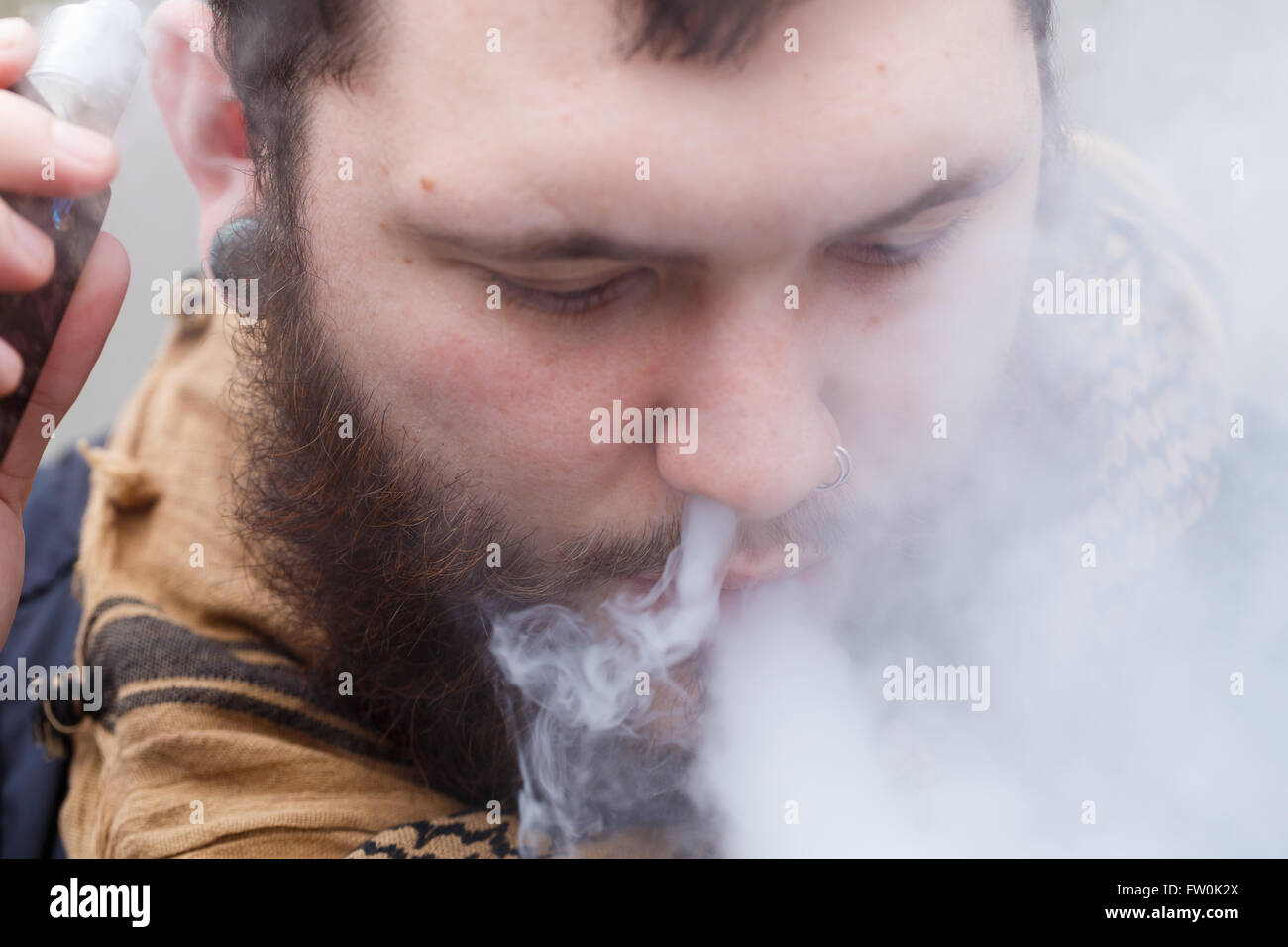 Urban lifestyle portrait of a man vaping in an urban environment with a custom vape mod device. Stock Photo