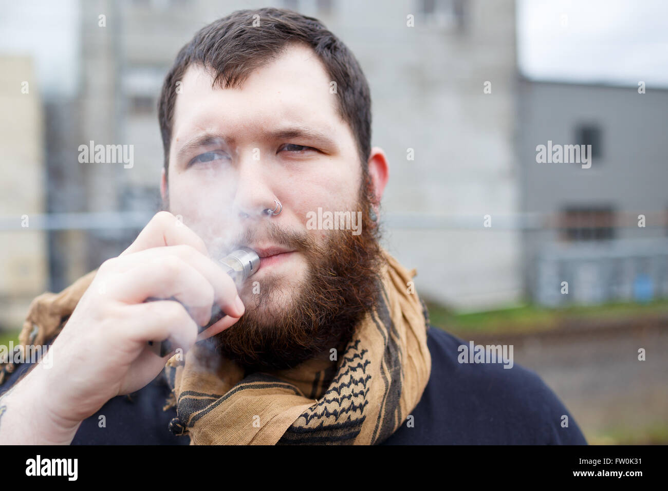 Urban lifestyle portrait of a man vaping in an urban environment with a custom vape mod device. Stock Photo