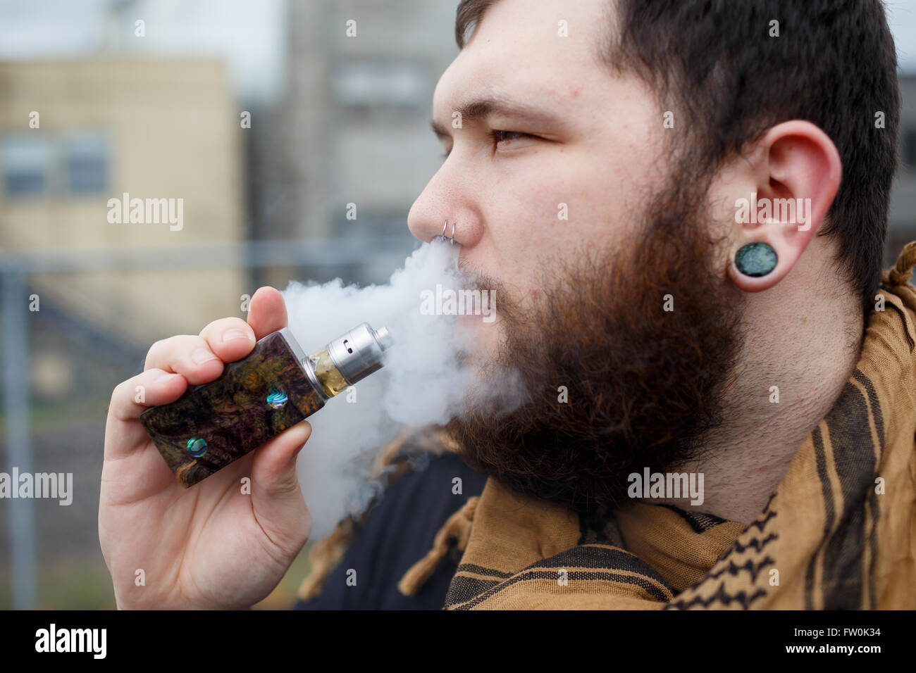 Urban lifestyle portrait of a man vaping in an urban environment with a custom vape mod device. Stock Photo