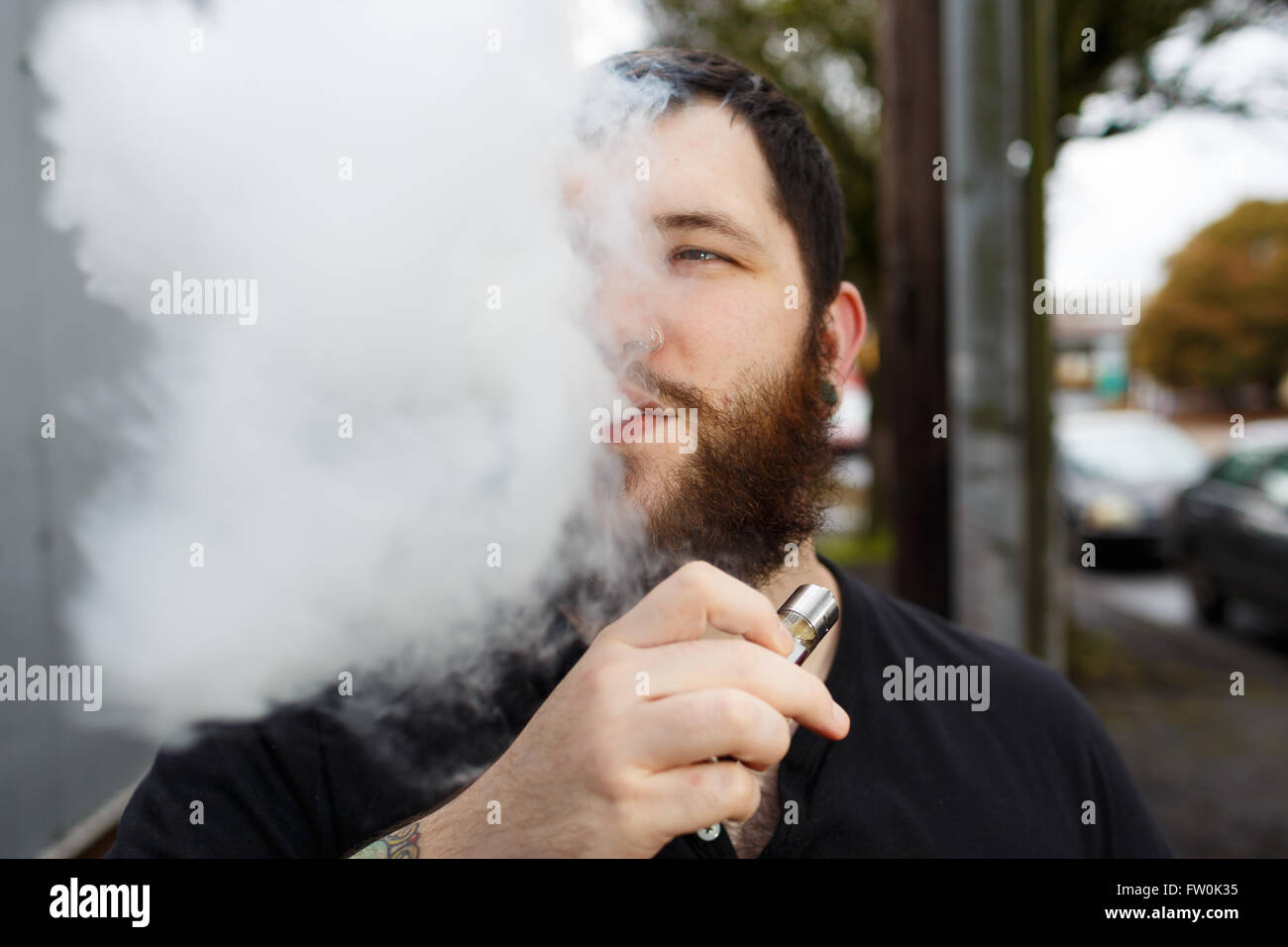 Urban lifestyle portrait of a man vaping in an urban environment with a custom vape mod device. Stock Photo