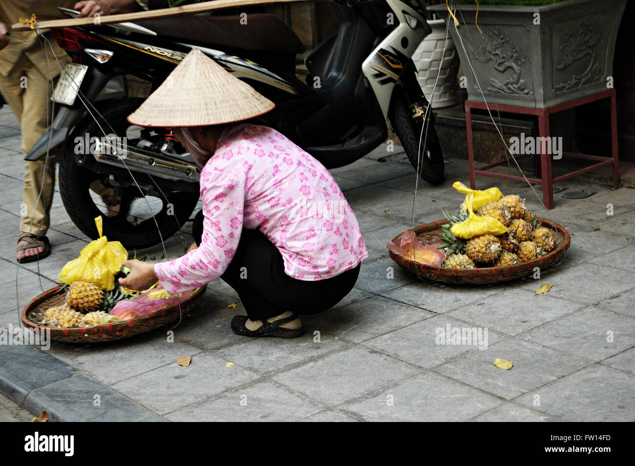 Vietnamese woman with typical conical hat selling pineapples in the old quarter of Hanoi, Vietnam Stock Photo