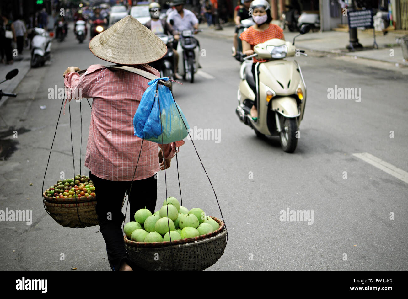 Woman street vendor with a typical conical hat walking in a street of Hanoi, Vietnam Stock Photo