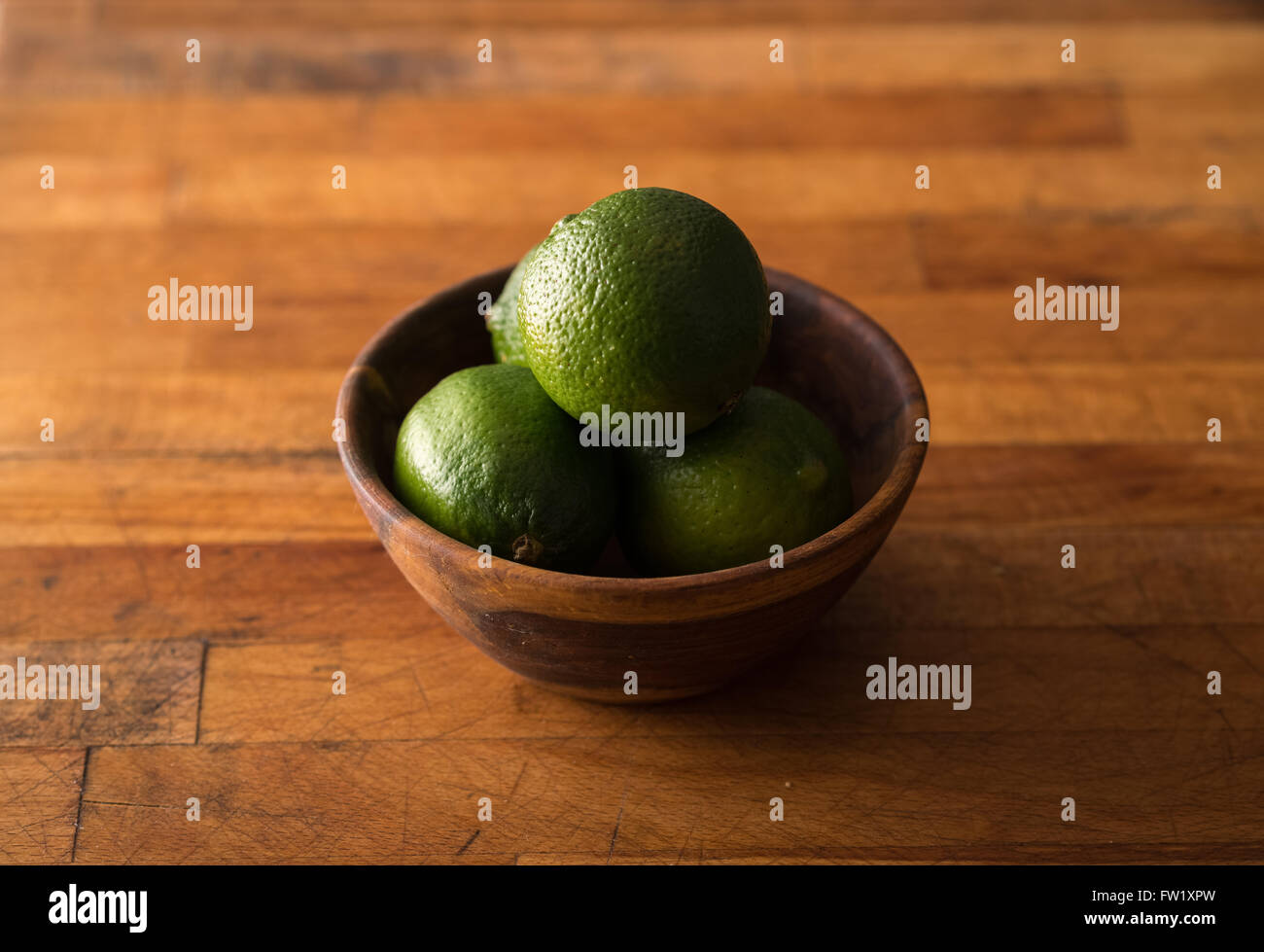 Raw whole limes in bowl on rustic wood Stock Photo