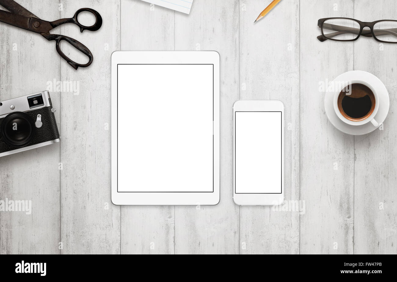 Tablet and smart phone with isolated white screen for mockup. Work desk with camera, glasses, coffee, notepad and pencil beside Stock Photo