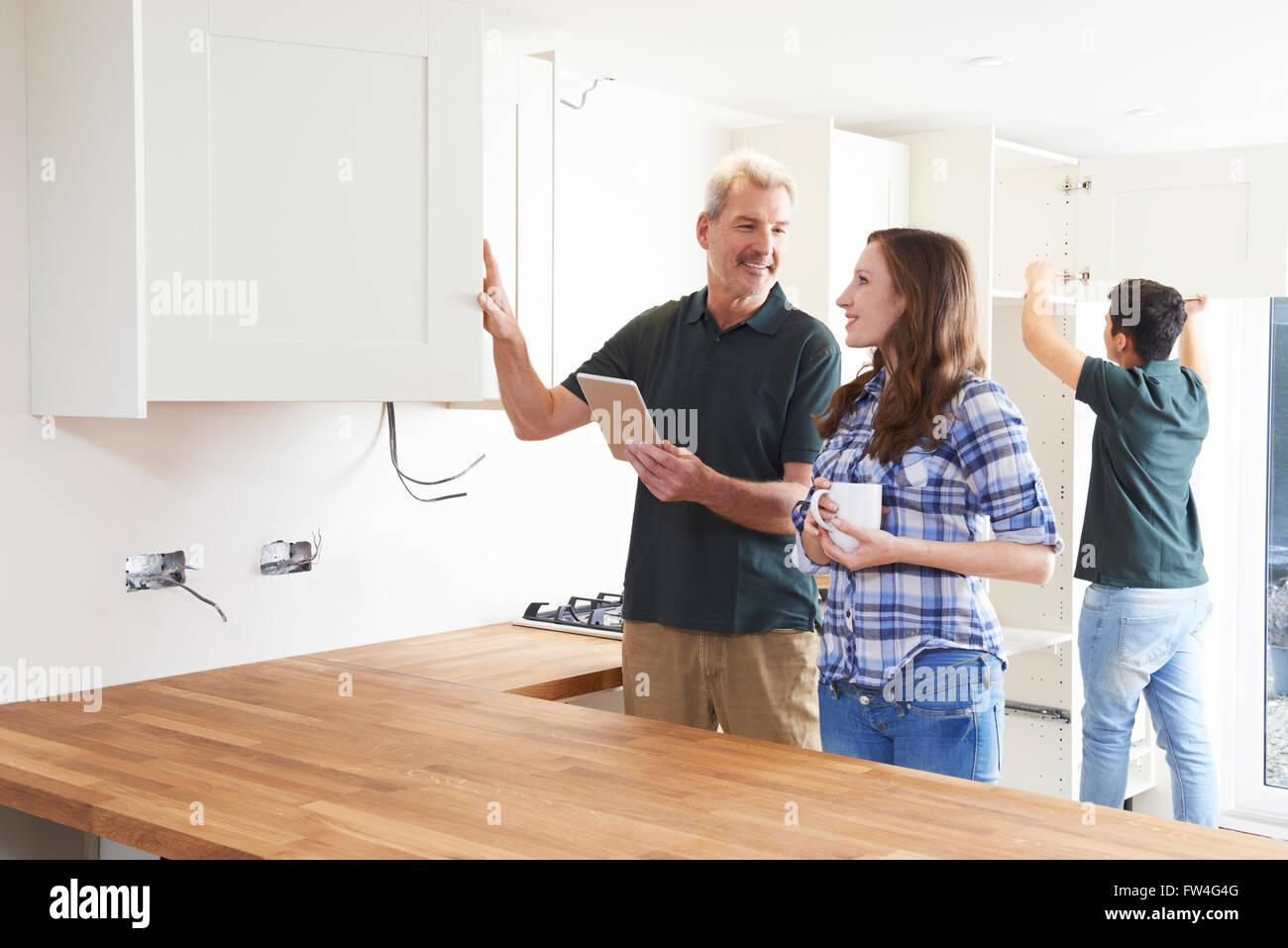 Woman With Carpenter Looking At Plans For Kitchen On Digital Tablet Stock Photo
