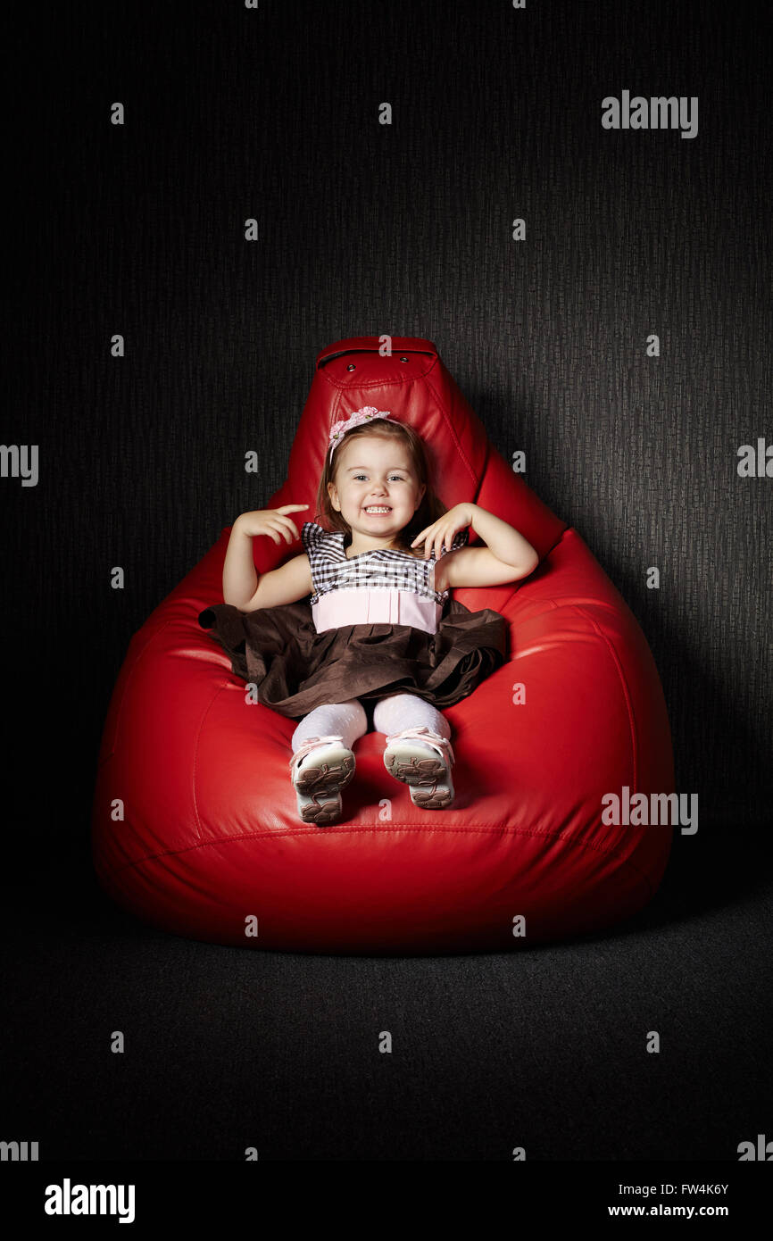 Little girl sitting on red beanbag Stock Photo - Alamy