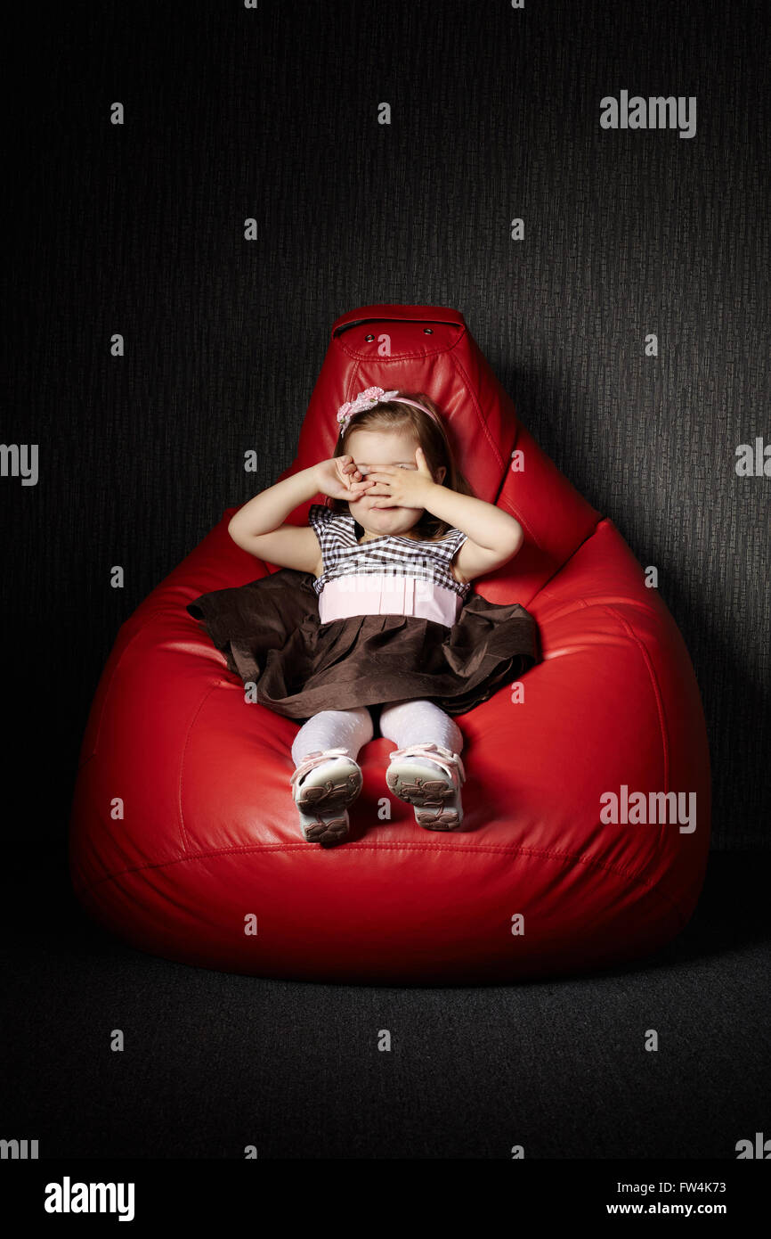 Little girl sitting on red beanbag Stock Photo - Alamy