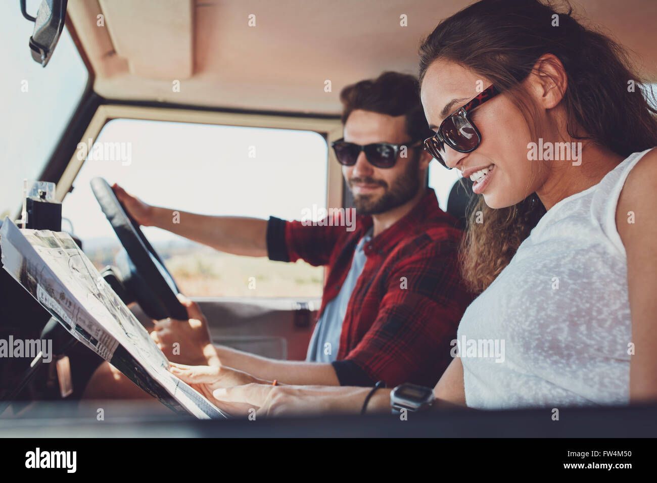 Side view of young couple reading a map for directions. Young man and woman in the car going on roadtrip. Stock Photo
