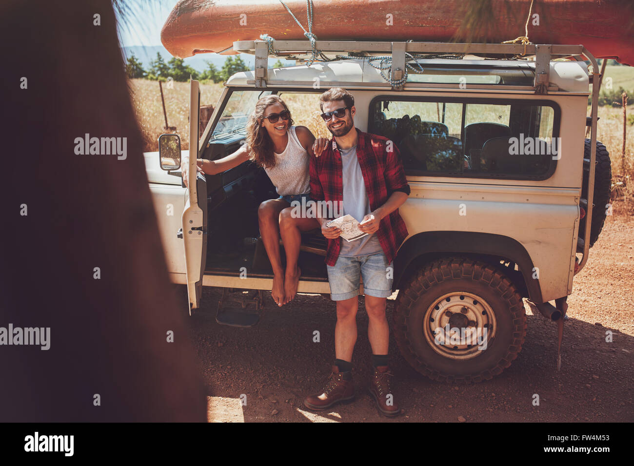 Portrait of happy young couple taking a break on roadtrip. Young man and woman enjoying on a road trip vacation. Stock Photo