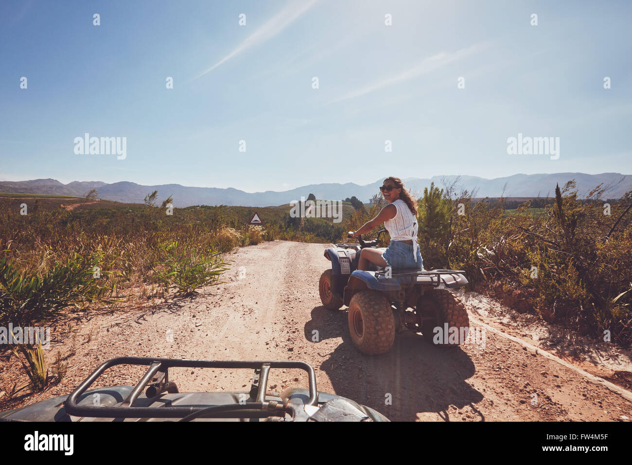 Young woman driving a quad bike on country road. Young woman on an all terrain vehicle in nature on a sunny day. Stock Photo