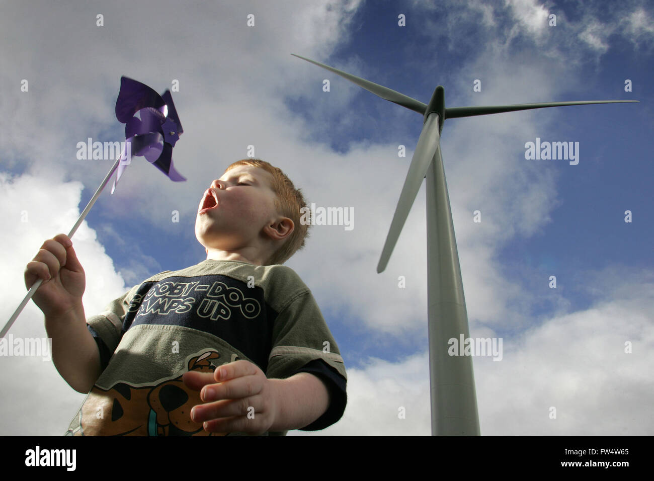 Boy blowing windmill at wind farm, Scotland Stock Photo