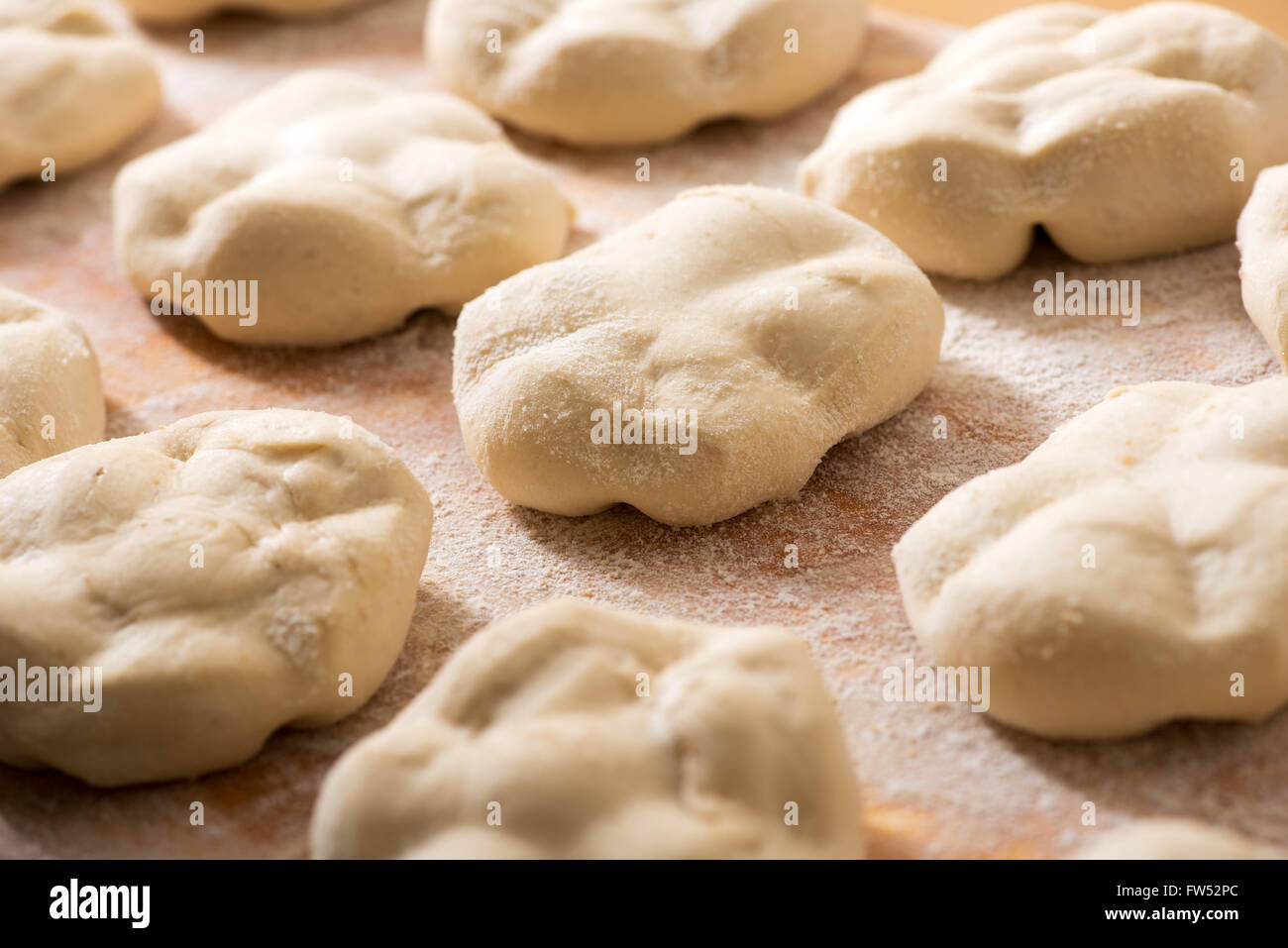 Fresh loaves of bread with specialist shapes laid out on a floured wooden bakery table, close up view with selective focus Stock Photo
