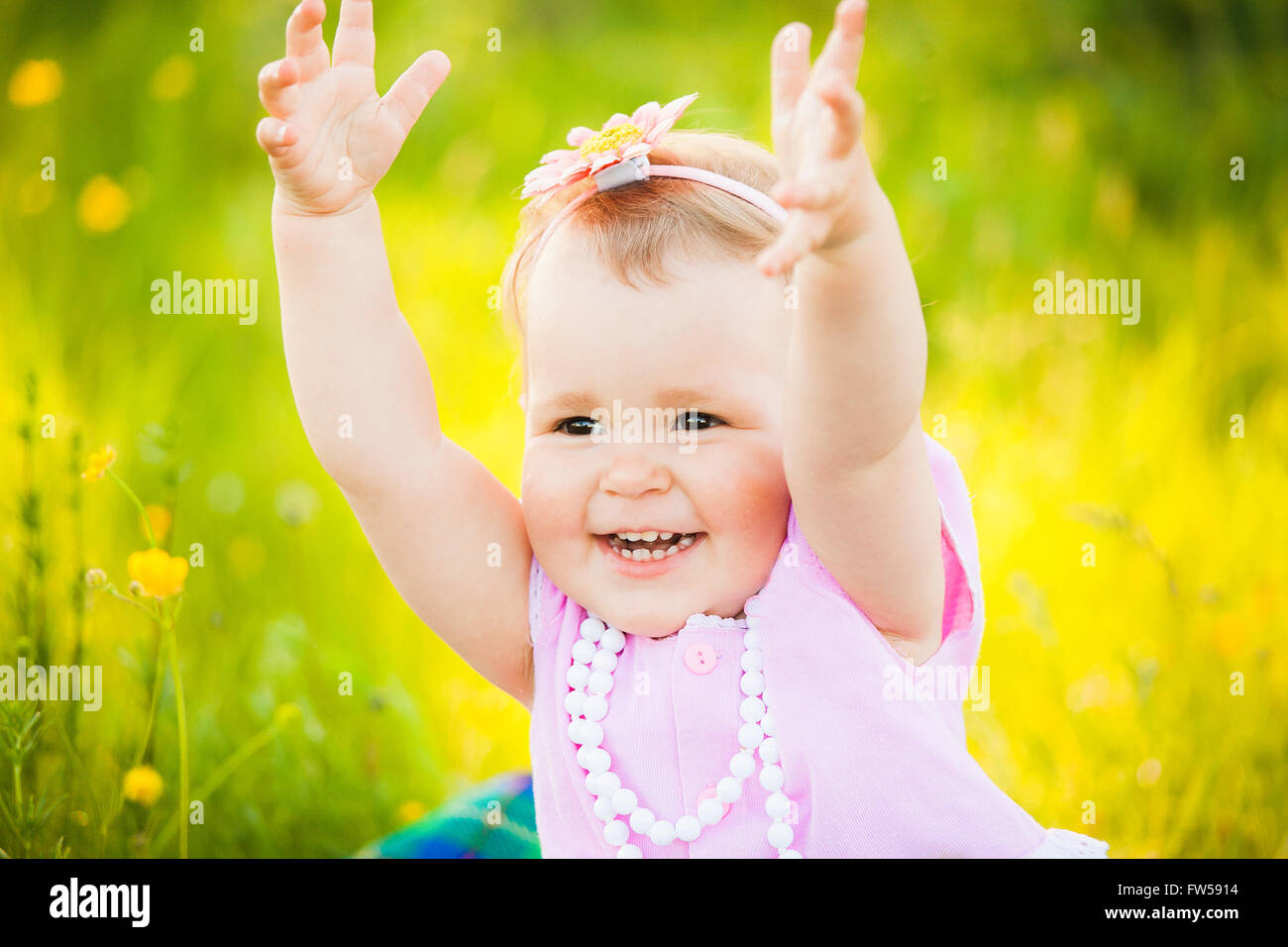 Portrait of playful funny child at sunny meadow background. Close up of happy smiling face of  little girl in pink dress. Little Stock Photo