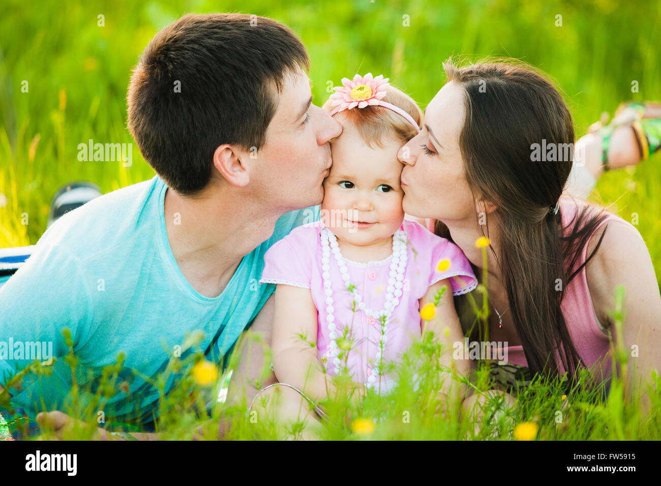 Mom and dad kissing cheeks of little daughter. Family portrait. Stock Photo