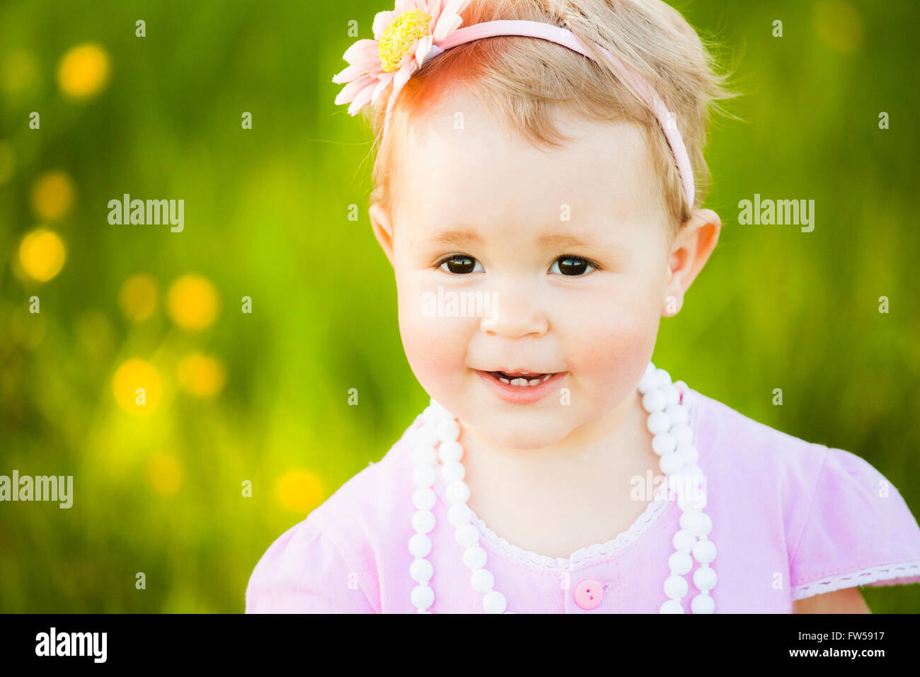 Portrait of playful funny child at sunny meadow background. Close up of happy smiling face of  little girl in pink dress. Little Stock Photo