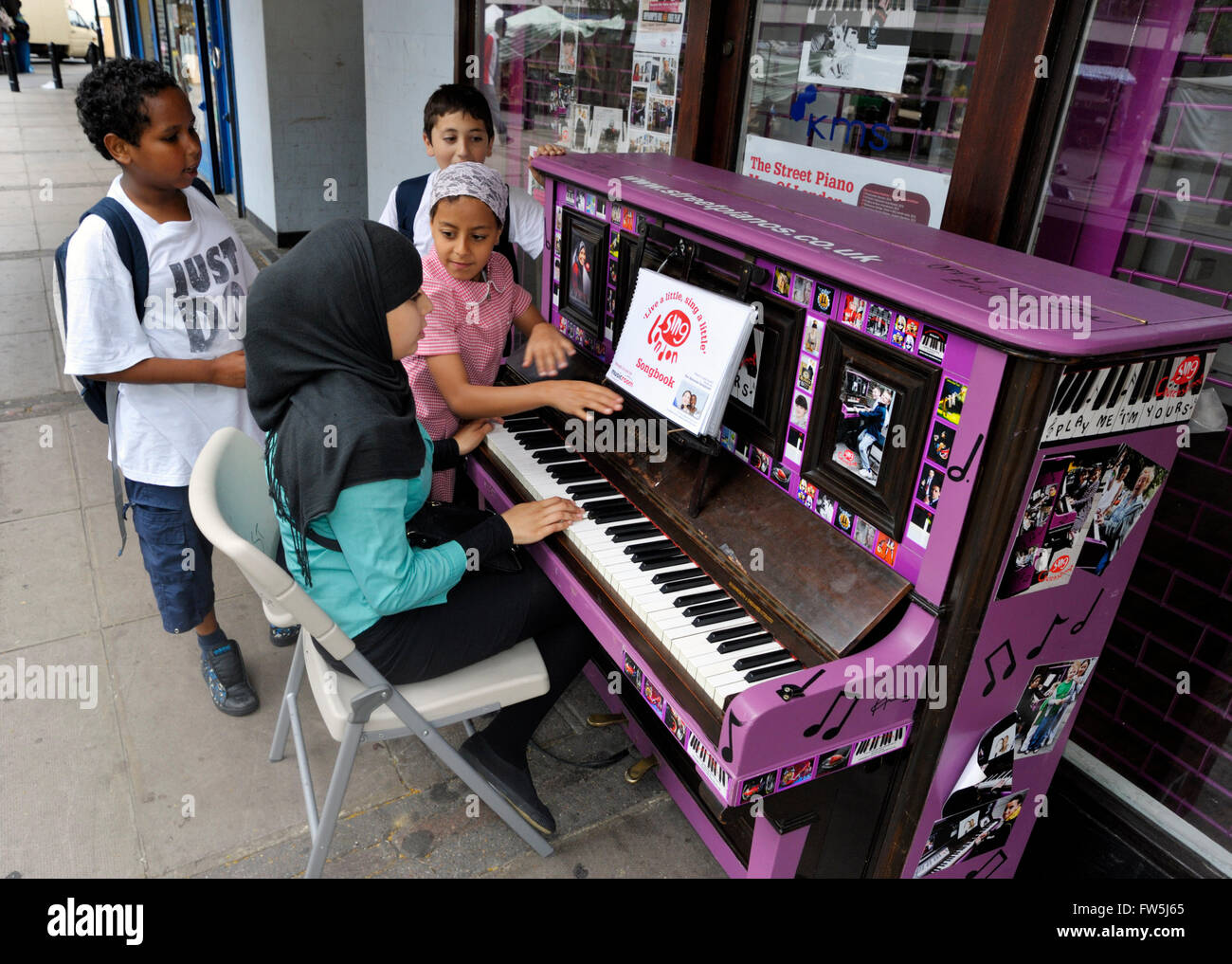 Asian children on street market playing old upright piano (by Chappell),  painted purple. Part of Streetpiano.co.uk 'Play me, I'm yours' scheme by  artist Luke Jerram, for Sing London and the City of