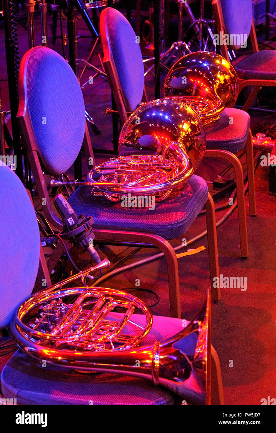 orchestral 'French' horns resting on chairs in rehearsal break, under coloured stage lighting