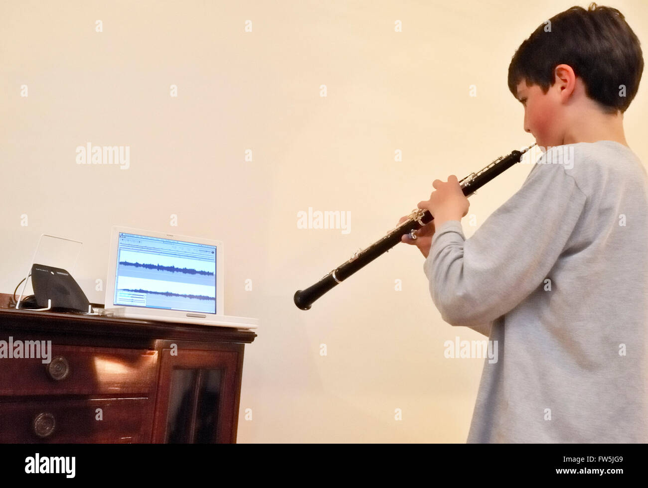 Teenage boy making a recording, playing the oboe, with music stand, computer running music recording software, and microphone. Stock Photo