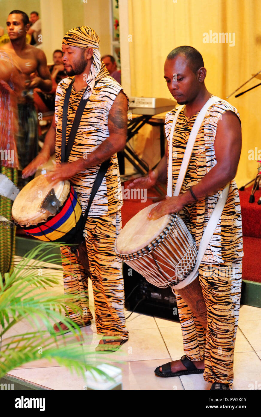 Sega drummers in Mauritius night club, playing djumbe / djumbe drumsfrom South-west Africa : sangban (medium drum); kenken, also tambour (small drum). Note the 'ears' that rattle. Sega is the national song and dance of Mauritius, extremely versatile. Accompanied by distinct instruments providing rhythm only without melody, such as the ravane (a thin, wide drum of goat's skin), the maravane (pebble-filled box rattling when shaken) and the triangle, the singer sings about the tribulations of love or the humorous side of life. Stock Photo