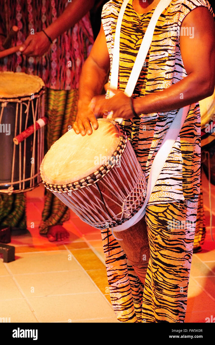 Sega drummer in Mauritius night club, playing djumbe / djembe drum from South-west Africa: sangban (medium drum). Sega is the national song and dance of Mauritius, extremely versatile. Accompanied by distinct instruments providing rhythm only without melody, such as the ravane (a thin, wide drum of goat's skin), the maravane (pebble-filled box rattling when shaken) and the triangle, the singer sings about the tribulations of love or the humorous side of life. Stock Photo