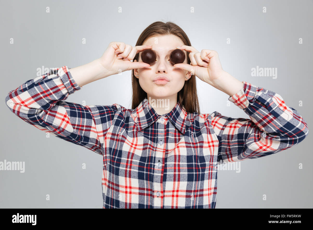 Beautiful amusing teenage girl in checkered shirt covered her eyes with round chocolate candies Stock Photo