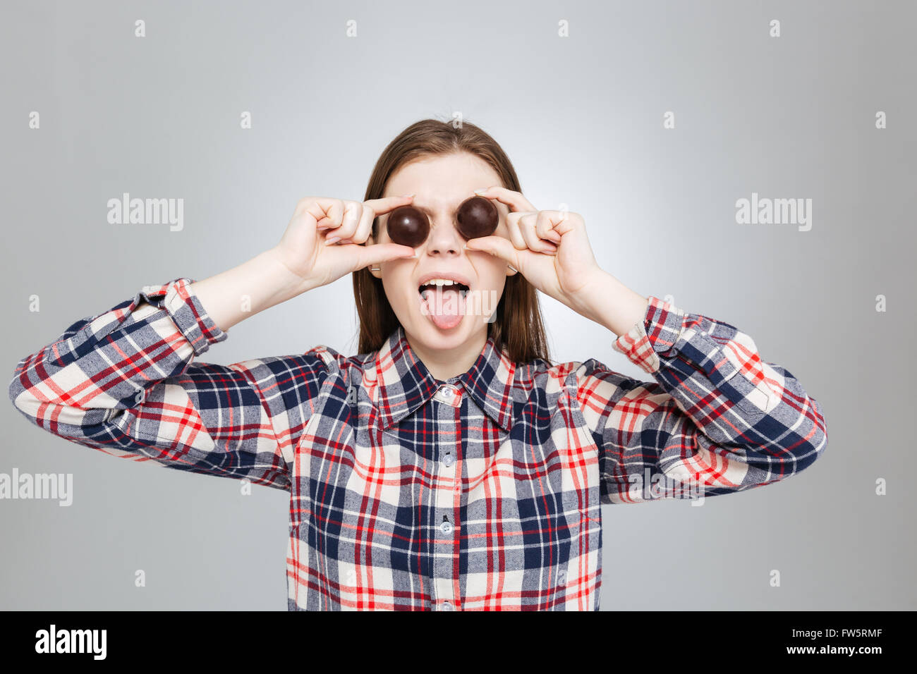 Pretty funny teenage girl in plaid shirt covered her eyes with  chocolate candies and showing tongue Stock Photo
