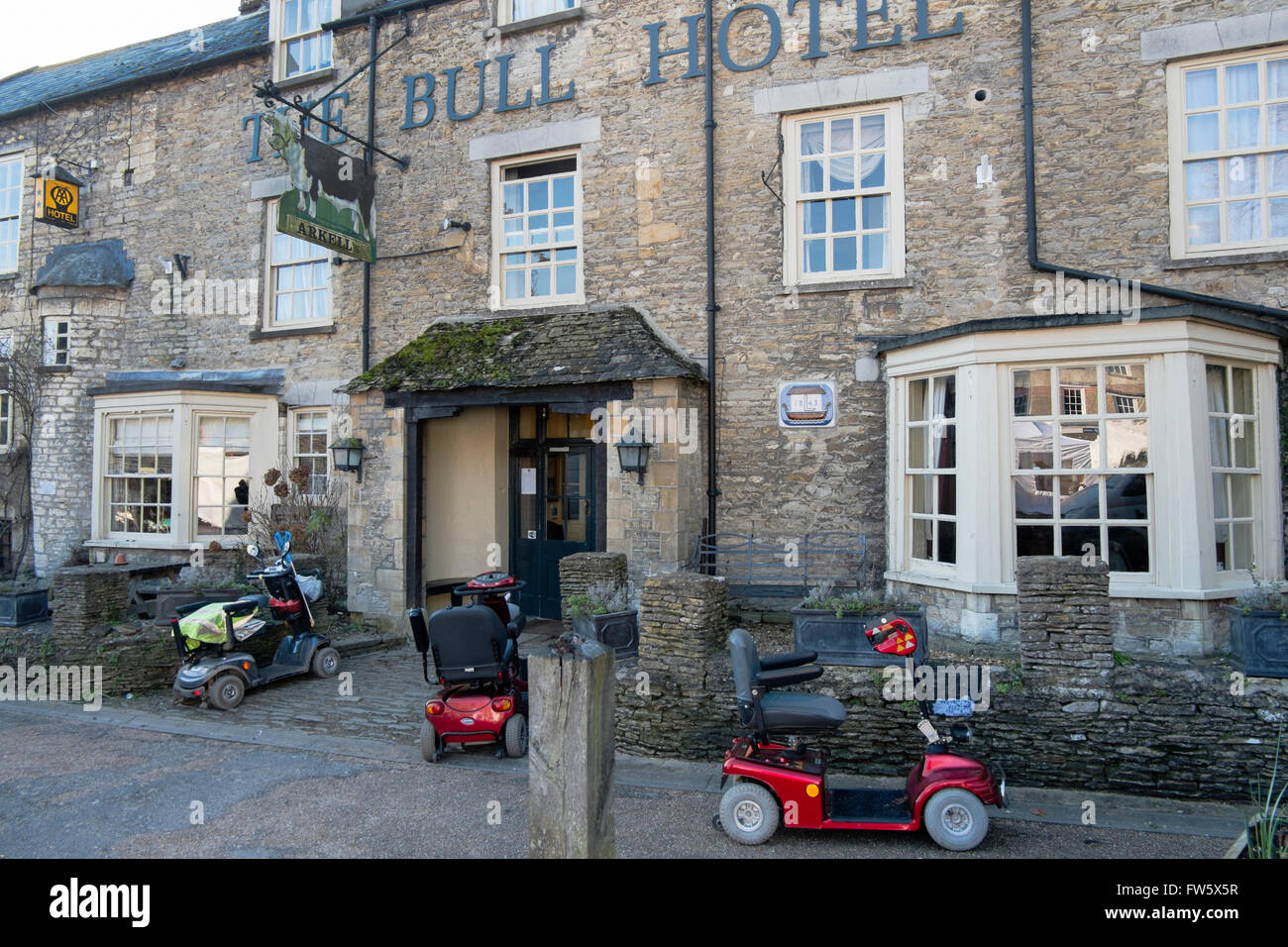 Three mobility scooters parked outside The Bull Hotel in the High Street in Fairford, Gloucestershire, UK Stock Photo
