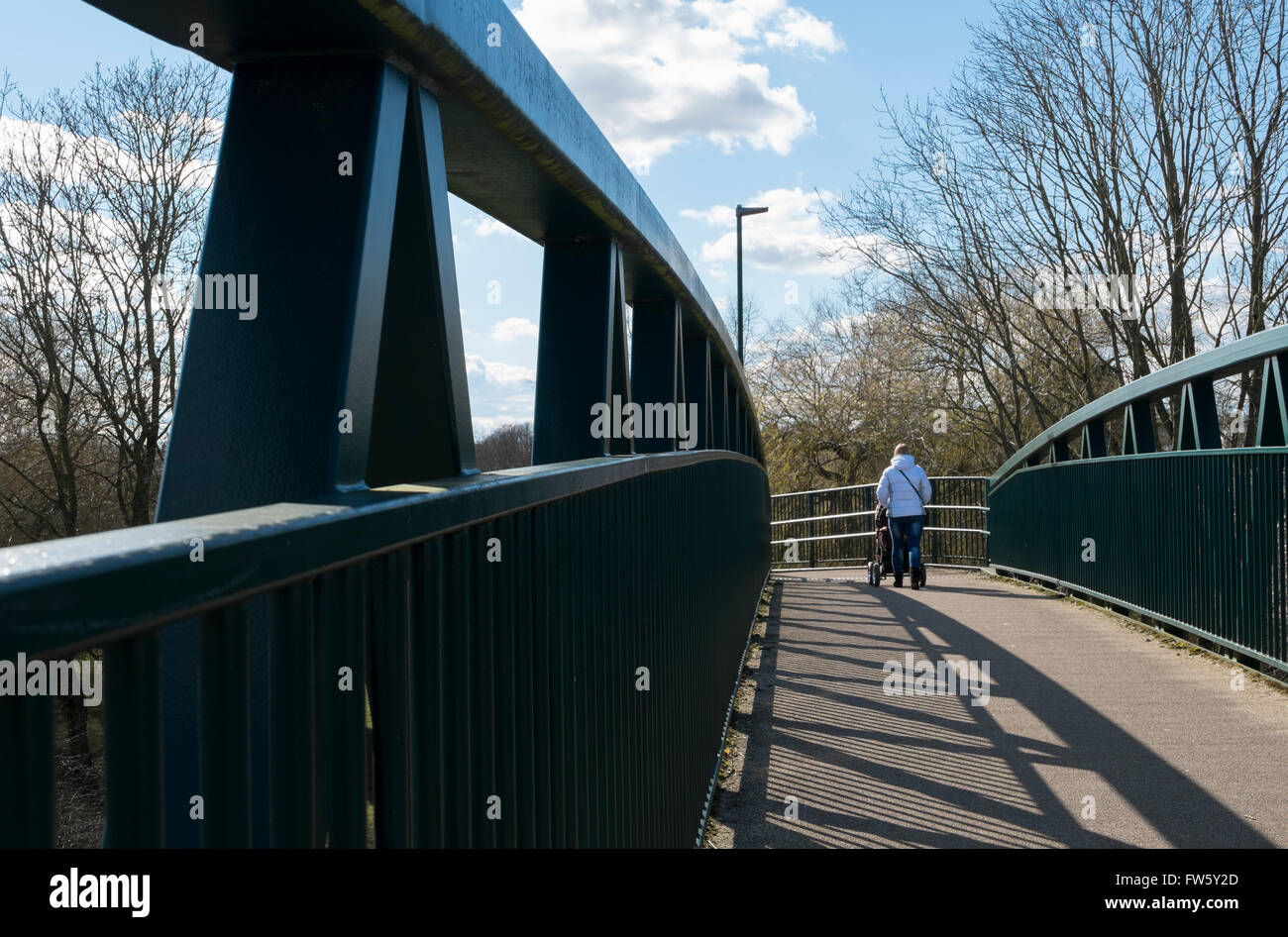 Woman with a pushchair walking over a footbridge over the A419 in Cirencester, Gloucestershire, UK Stock Photo