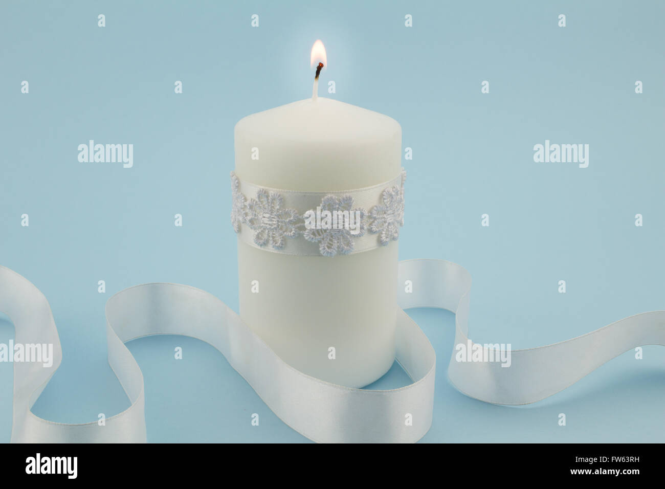 Close up photo of single white lit candle isolated with white satin
