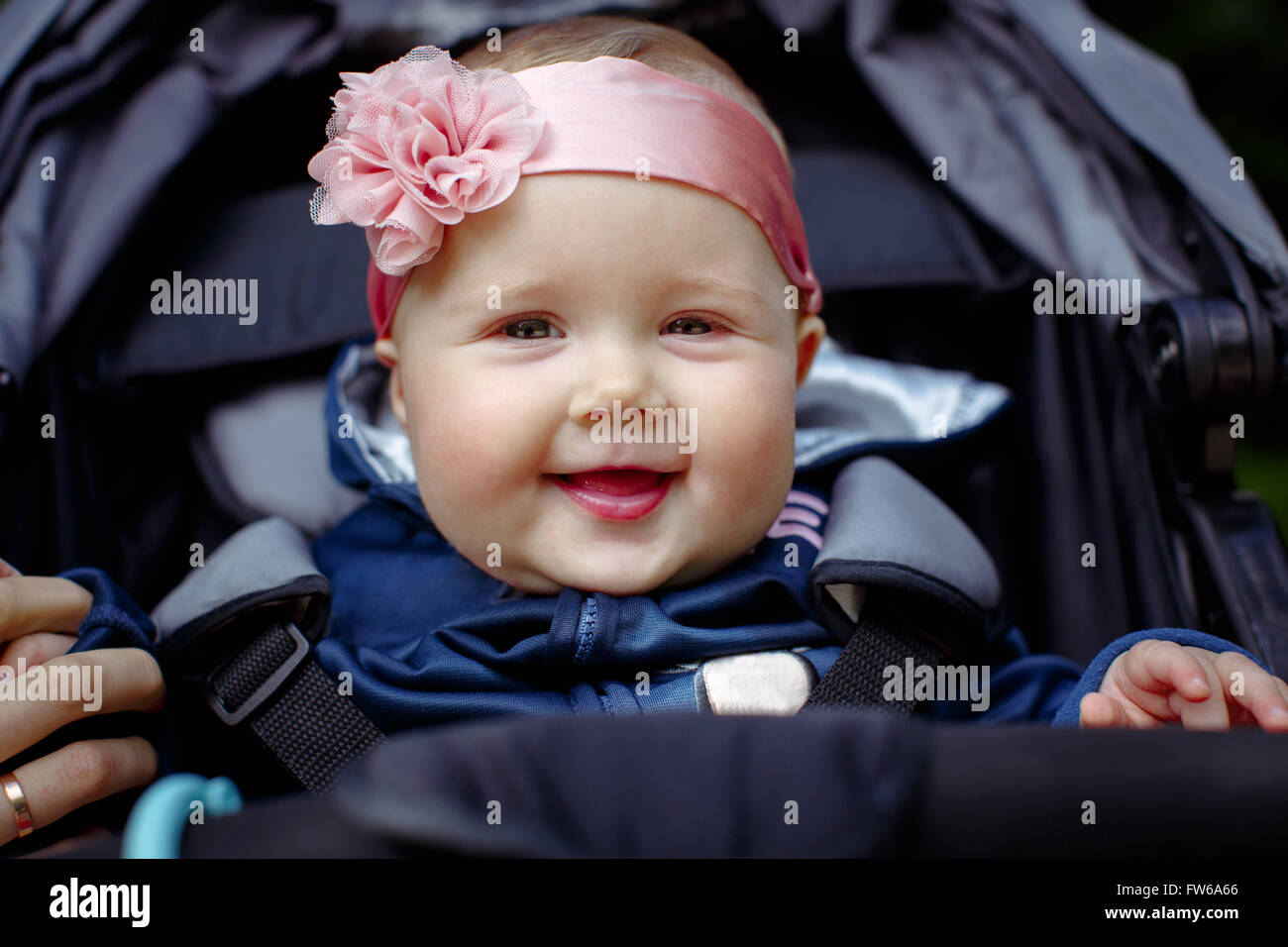 Baby sitting in a baby carriage, holding my mother's finger, a bandage on his head with a pink flower. Baby smiling and looking Stock Photo