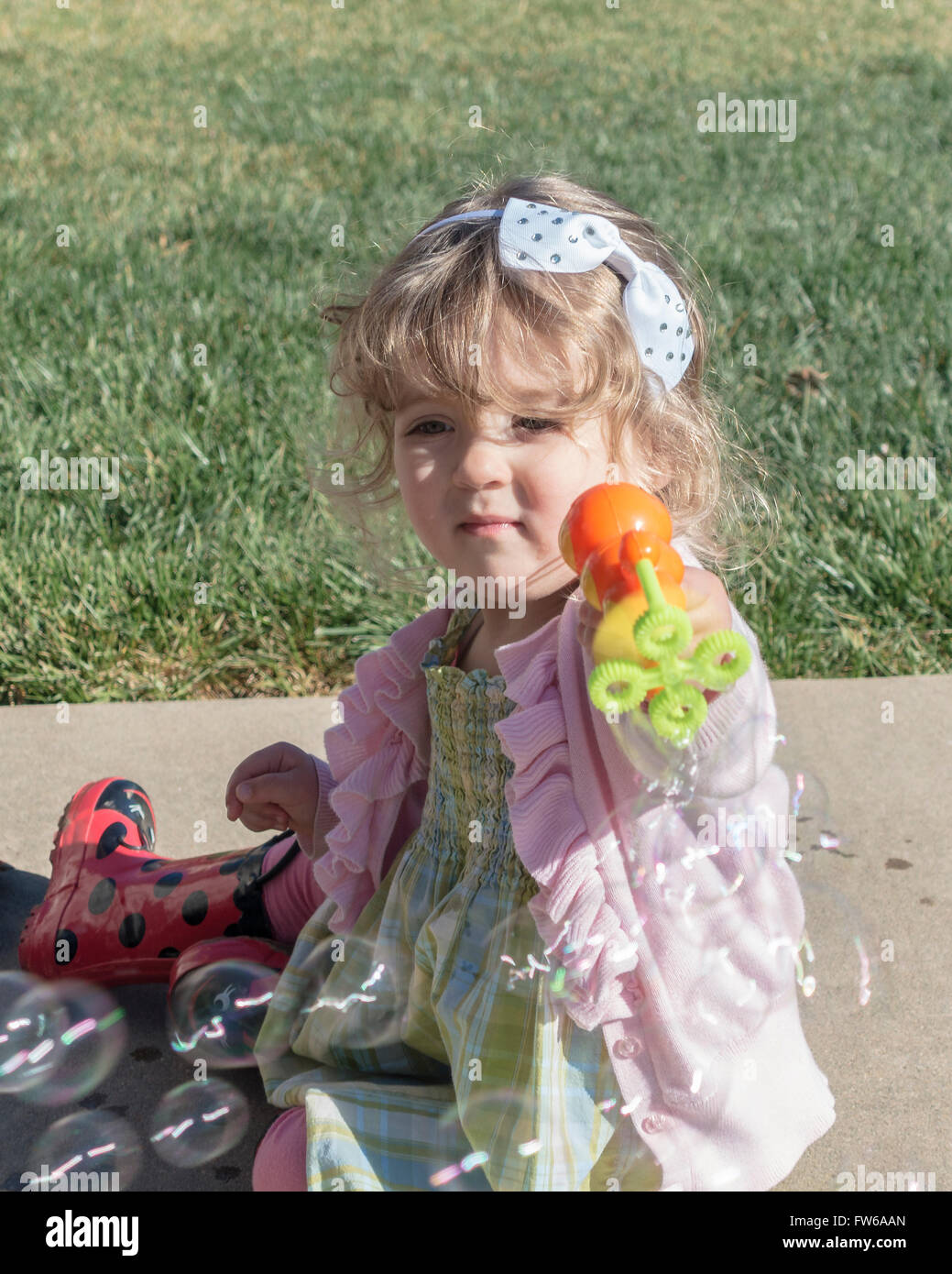 A 2 year old Caucasian toddler girl uses a toy to make soap bubbles. Stock Photo