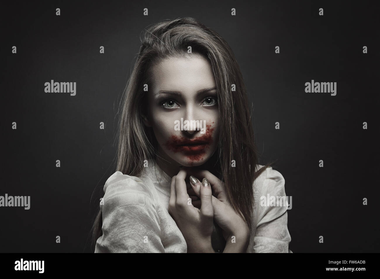 Beautiful vampire with innocent eyes but mouth dirty of blood . Halloween and horror Stock Photo