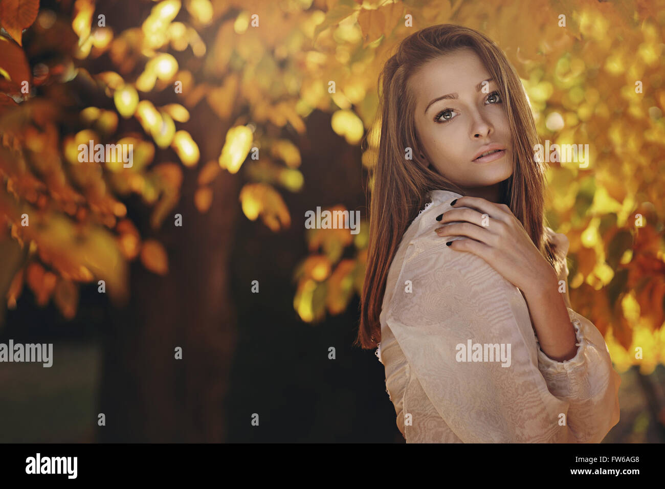 Beautiful young woman posing with autumn leaves in background Stock Photo