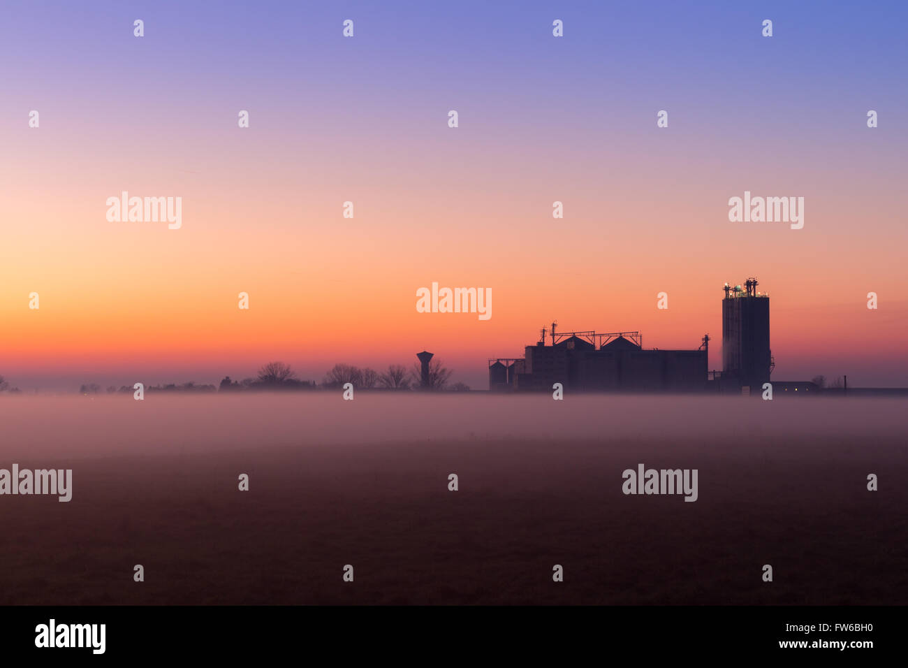 Industrial foggy landscape, silhouette of old factory against the sunset sky and the mist at blue hour at night Stock Photo