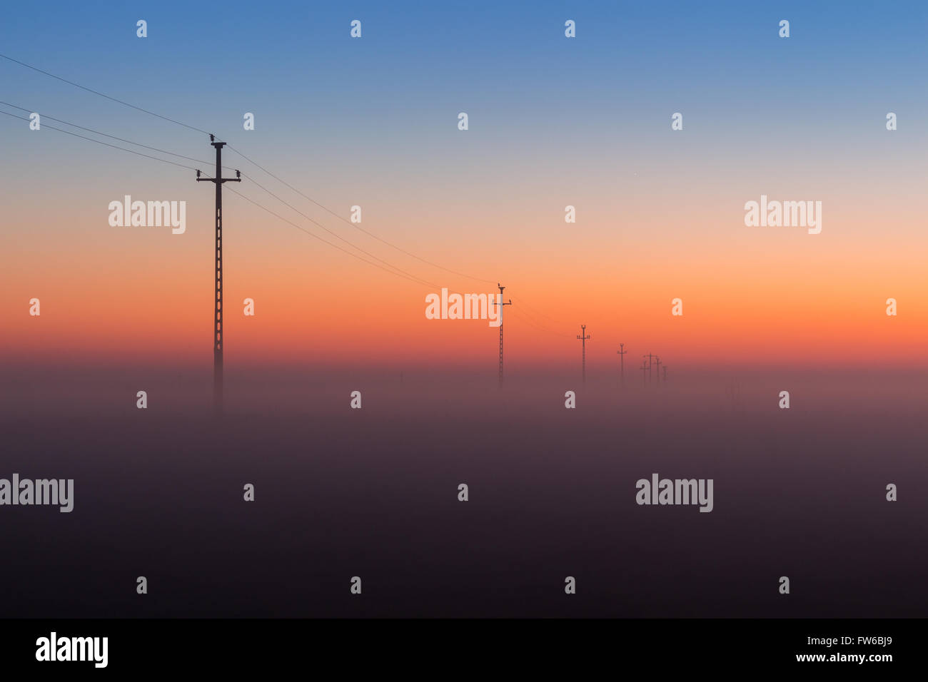 Electrical Power Lines and Pylons disappear over the horizon with Misty Sunrise, Sunset Stock Photo