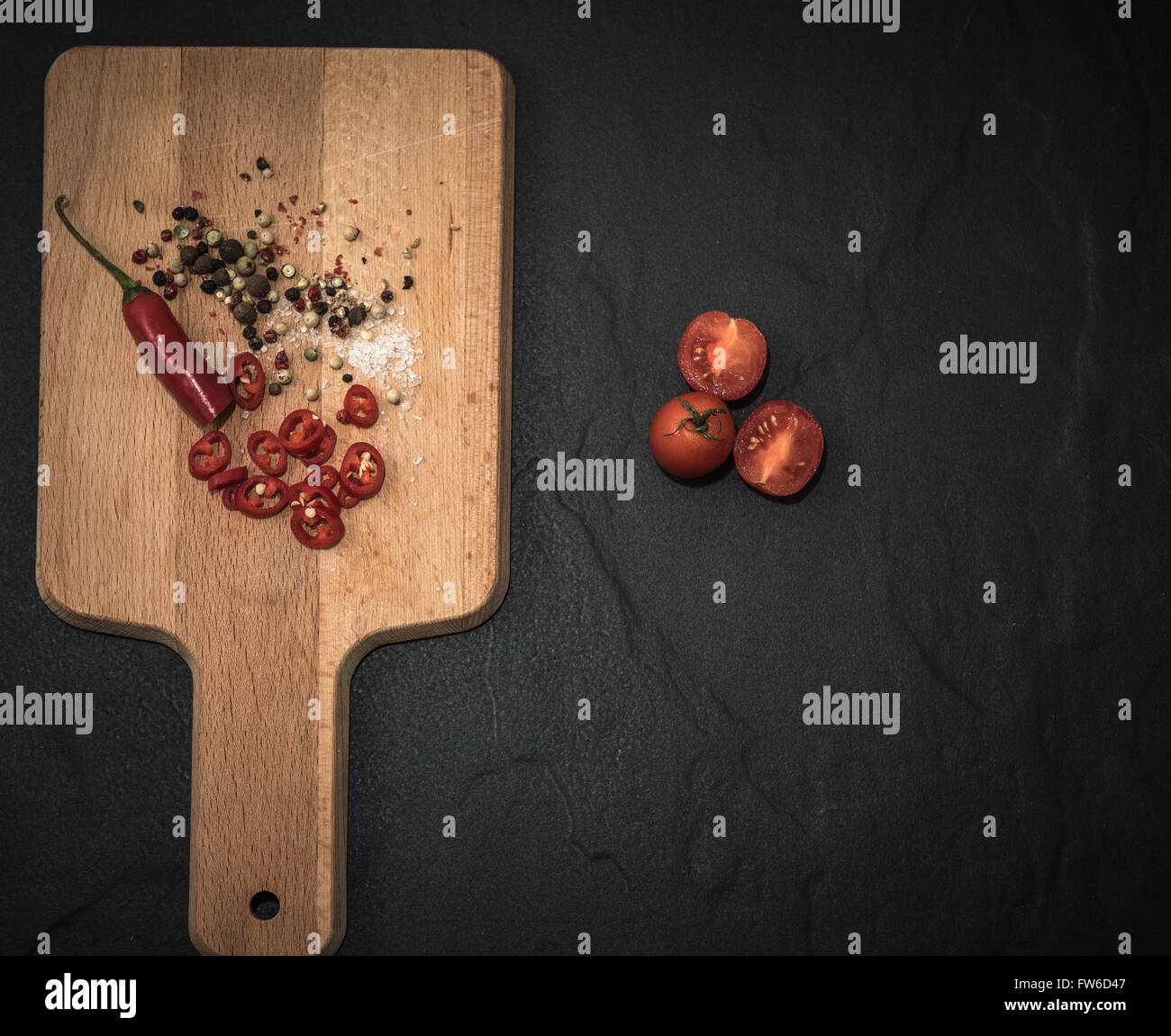 Rustic wooden chopping board on a Black slate background red chili ...
